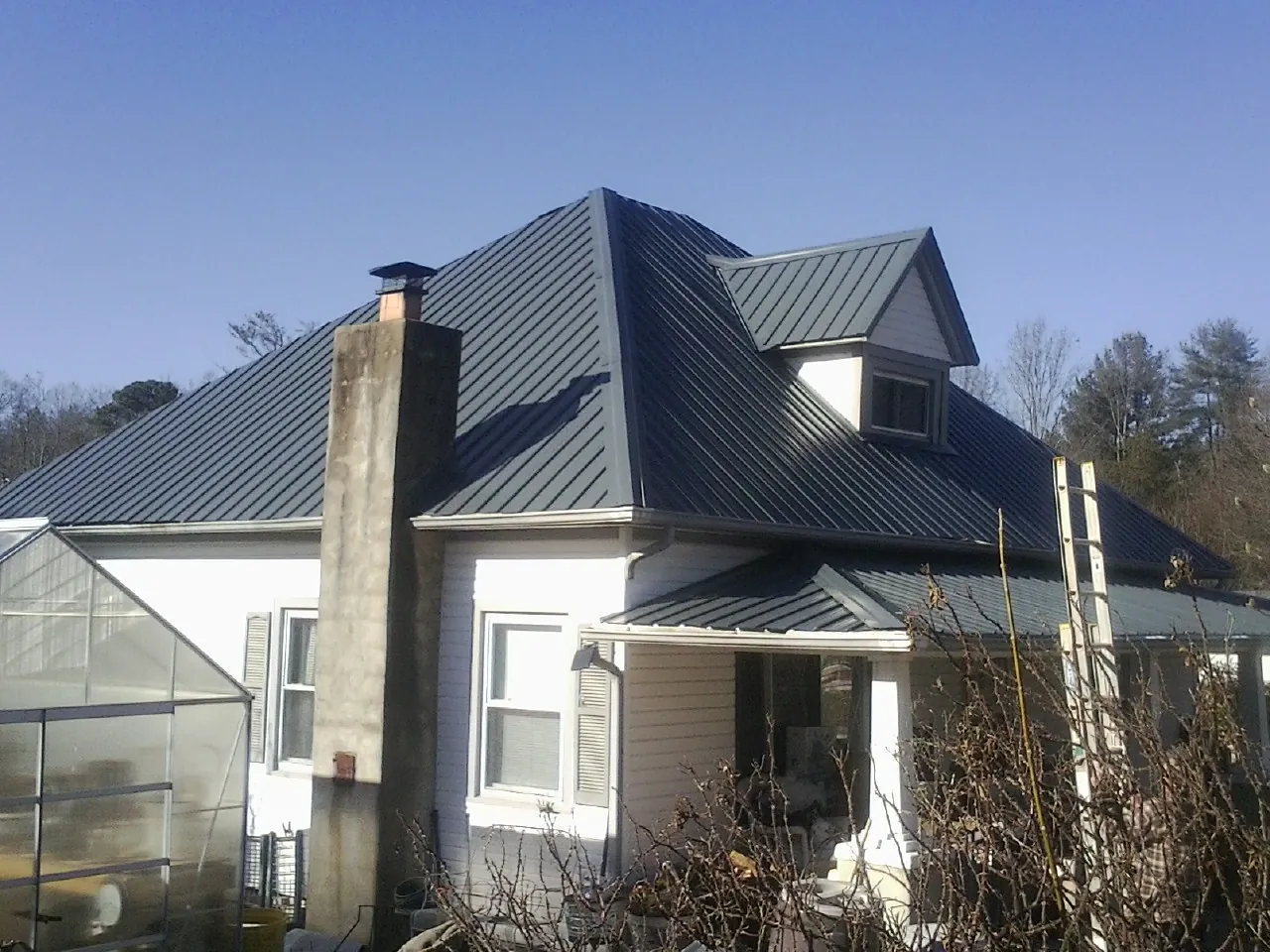 Dark blue standing seam metal roof on a white farmhouse with dormer — Slate & Tile Roof Repair by Roofing Brothers in Alkol