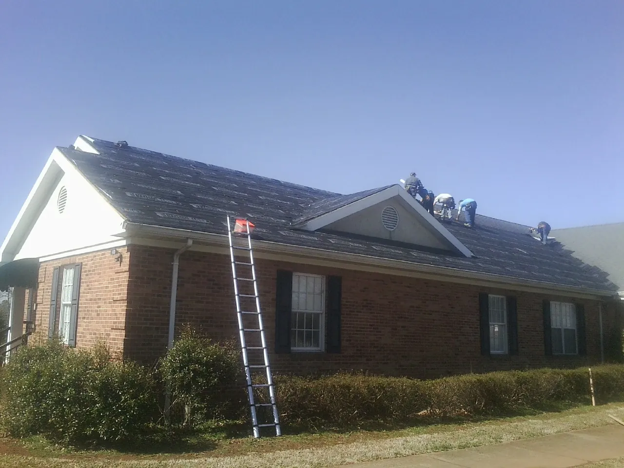 Crew tearing shingles off a brick ranch roof with a ladder set — Emergency Roof Repair work by our crew in Alkol