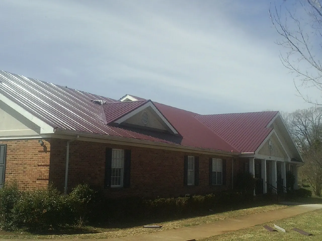 Red metal roof with gabled entries on a long brick building, from a Hail Damage Roof Repair job in Alkol