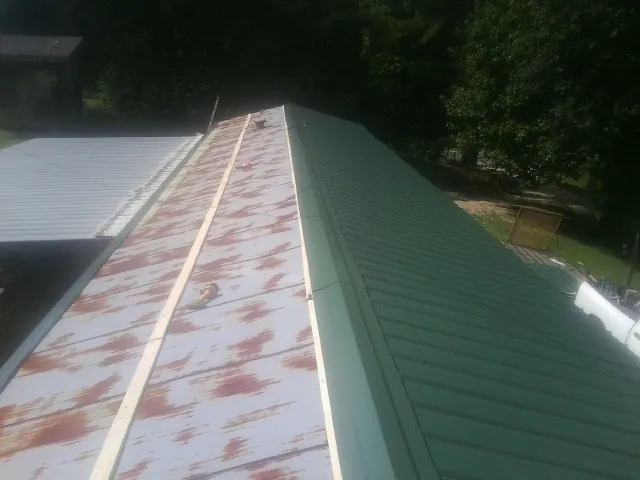 Old rusted panels beside newly installed green metal roofing — Wind Damage Roof Repair by Roofing Brothers in Alkol
