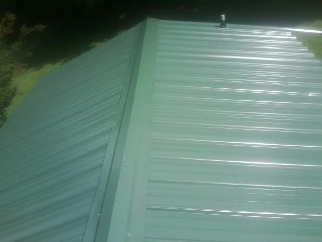 New green metal panels meeting at the ridge of a roof — Flat Roof Repair work by our crew in Alkol