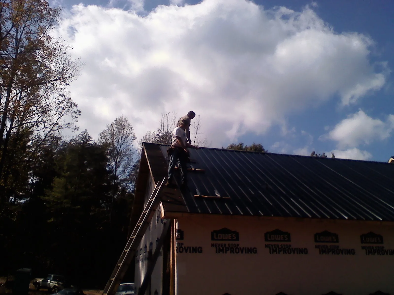 Roofer fastening dark metal panels high against a cloudy sky, from a Roof Inspection job in Alkol
