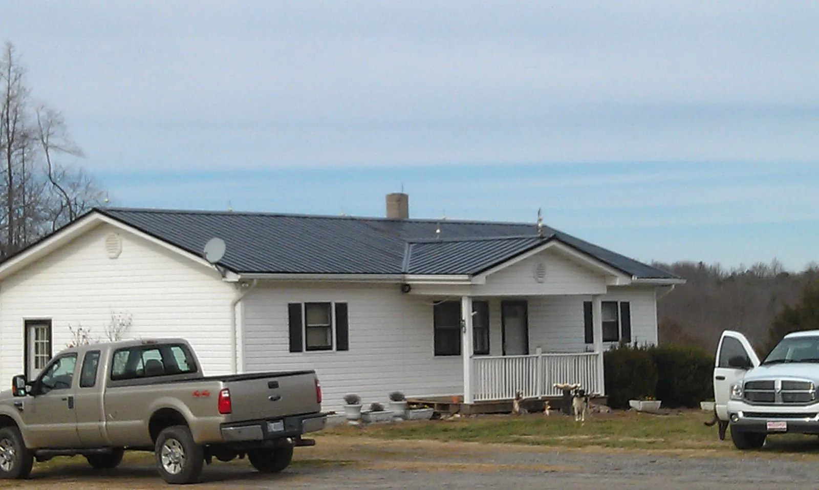 Finished dark metal roof on a white ranch home with work trucks parked in Alkol