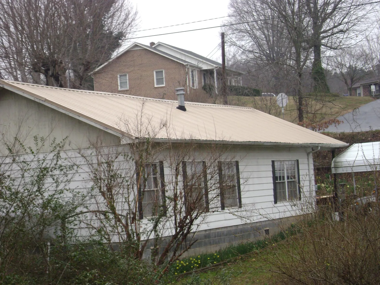 Tan metal roof on a white sided house set into a hillside — Commercial Roofing by Roofing Brothers in Alkol